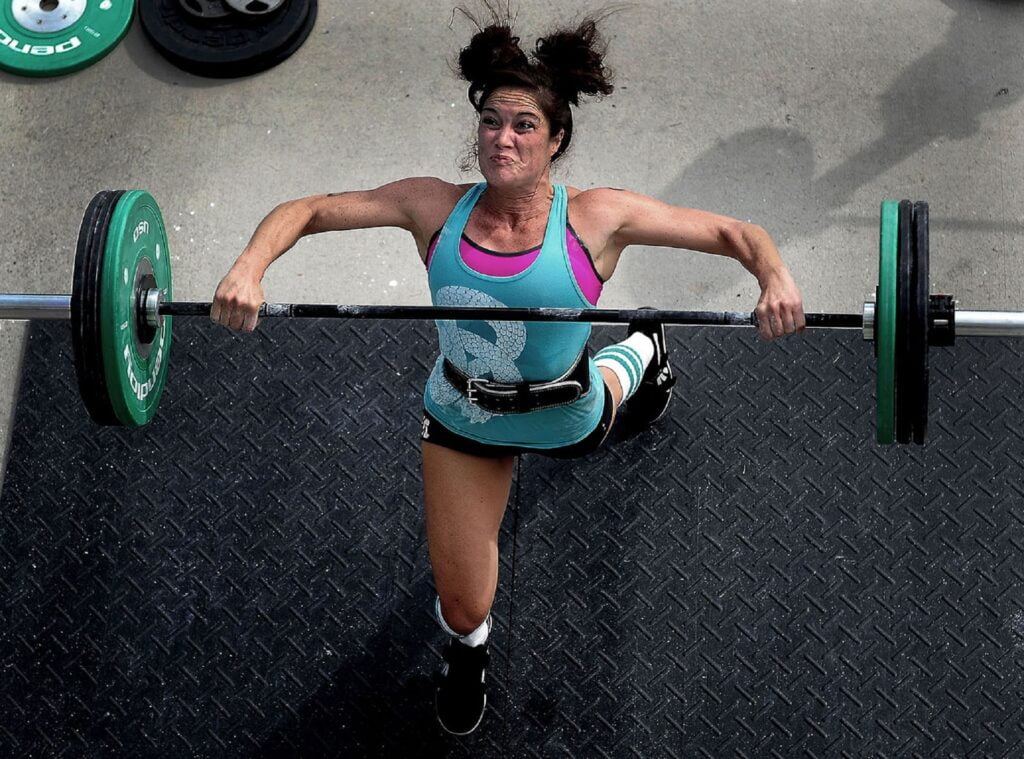 A female Olympic weightlifter lifts a barbell.